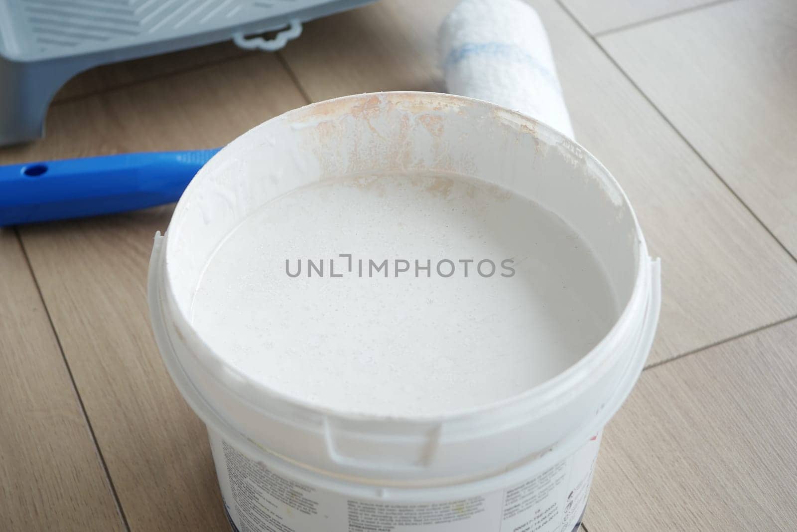 A bucket of white paint sits on a wooden floor, tools nearby hint at work.