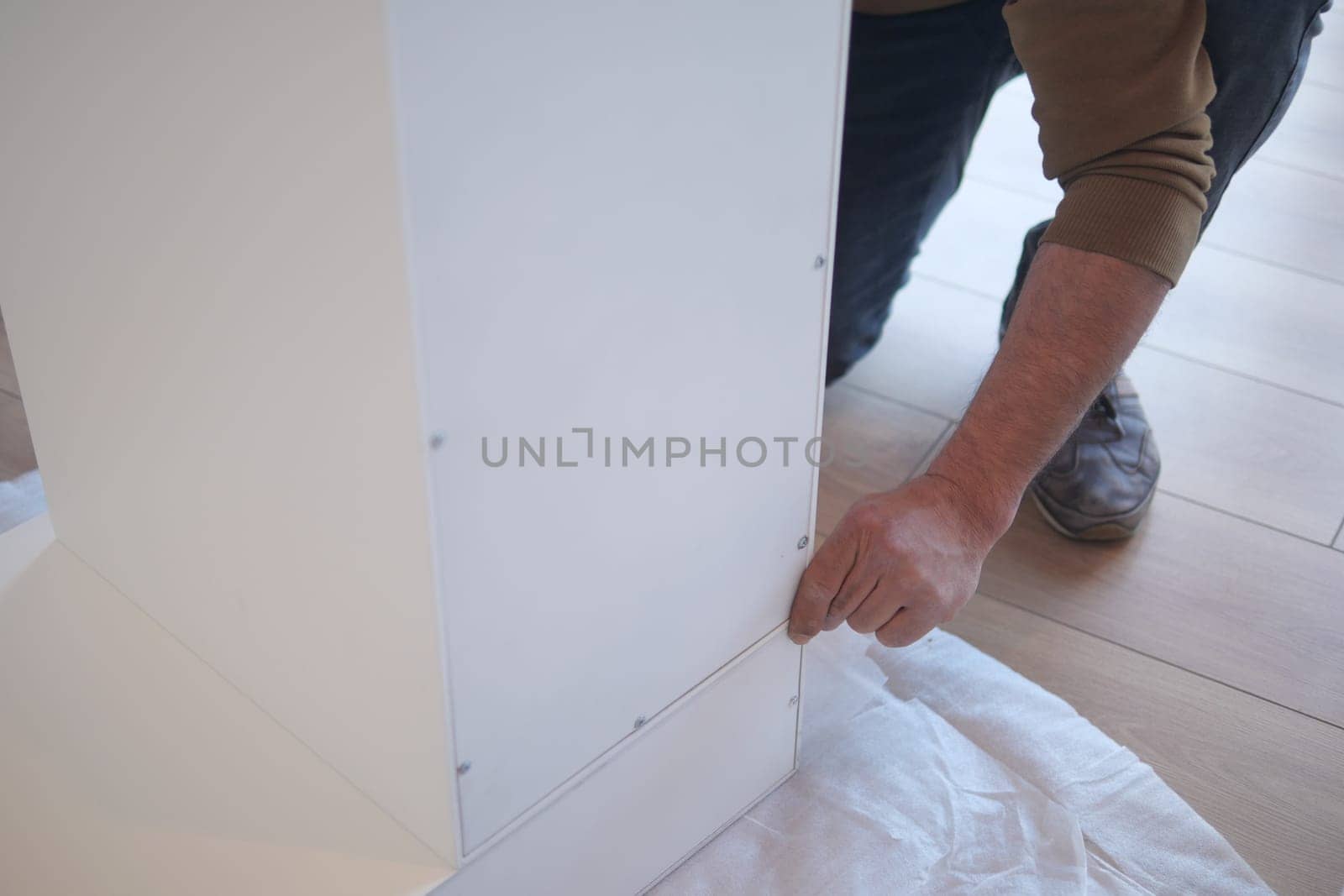 A person is assembling a white furniture piece in a bright room.