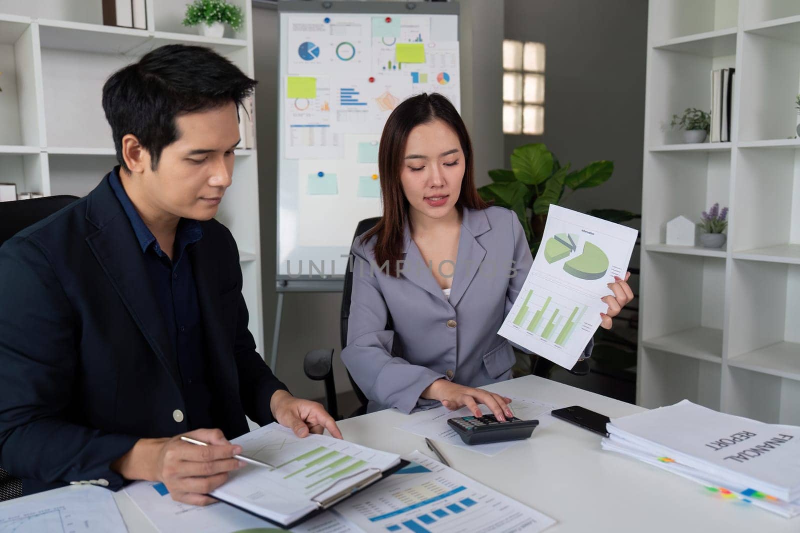 A focused meeting between two professionals, one presenting analytical charts while the other takes notes, symbolizing effective communication and analysis.