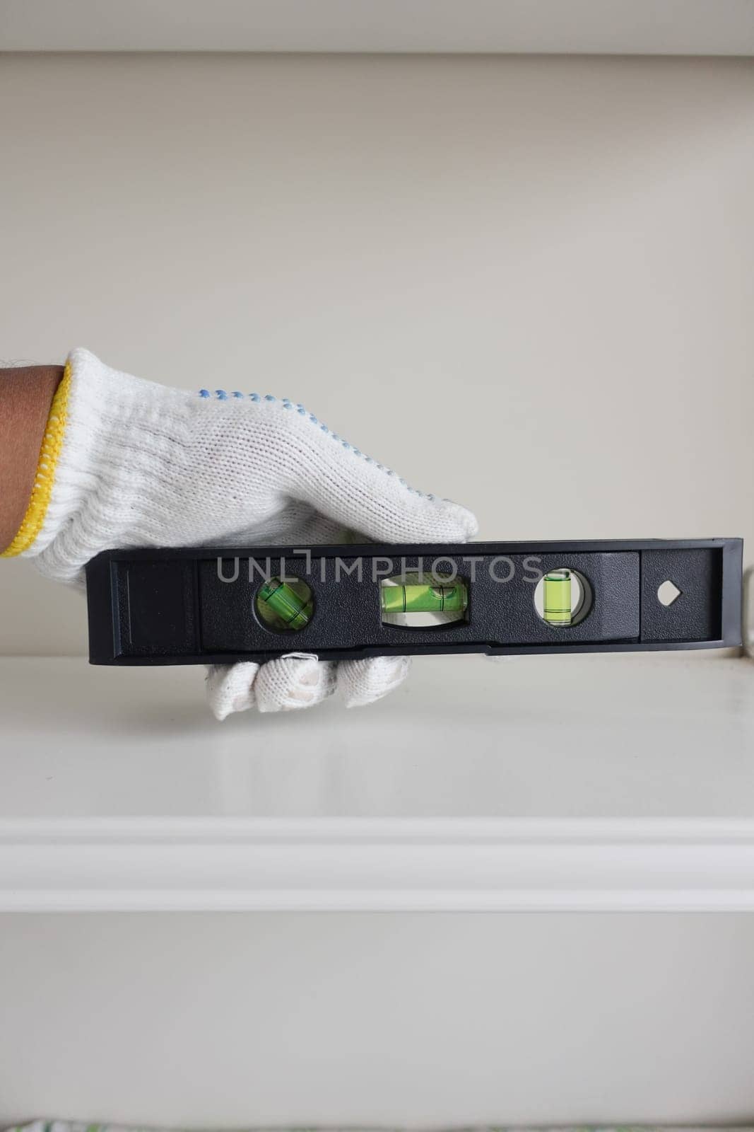 A hand wearing a glove holds a leveling tool to measure shelf balance.