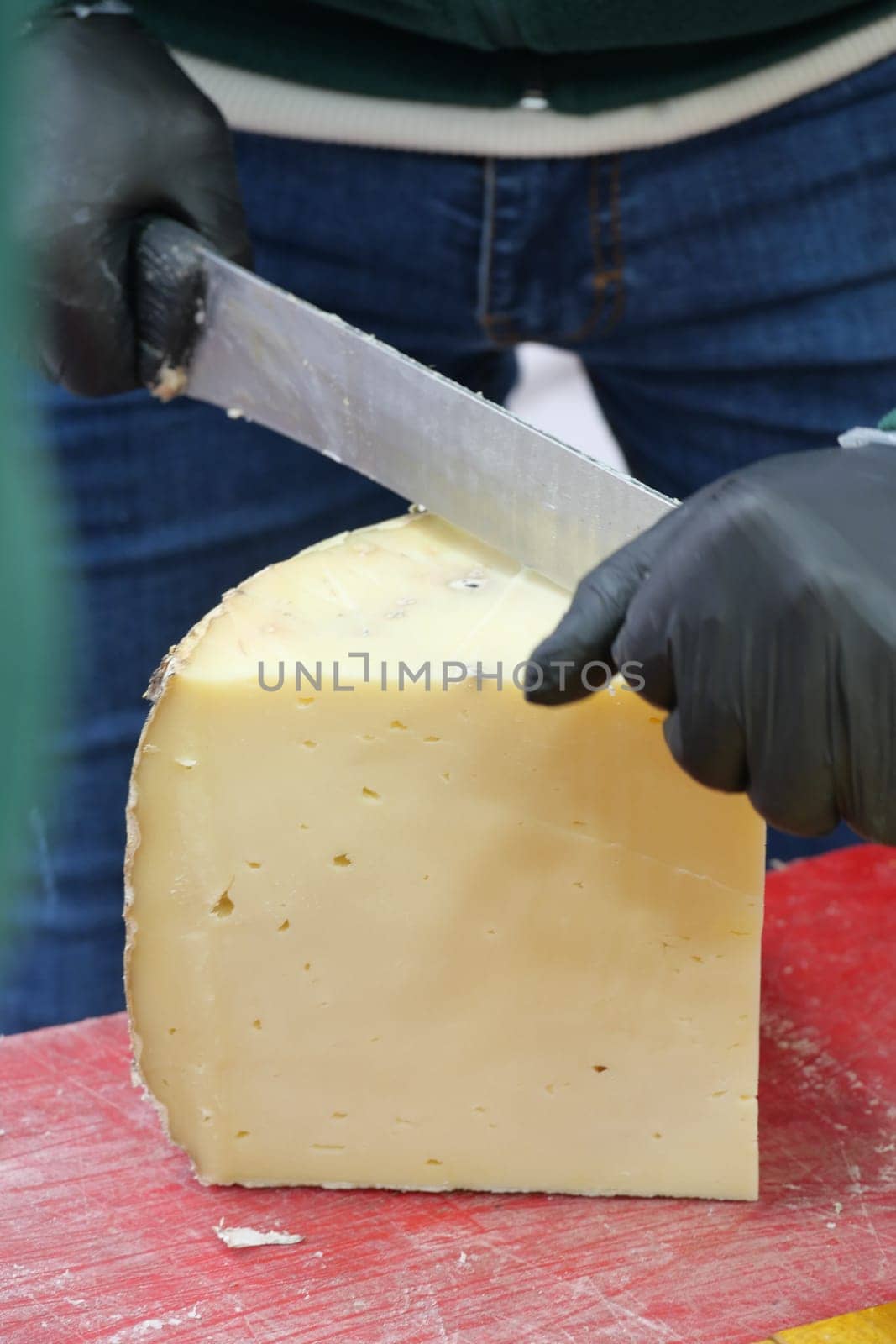 A person is skillfully cutting a large block of cheese at a market.