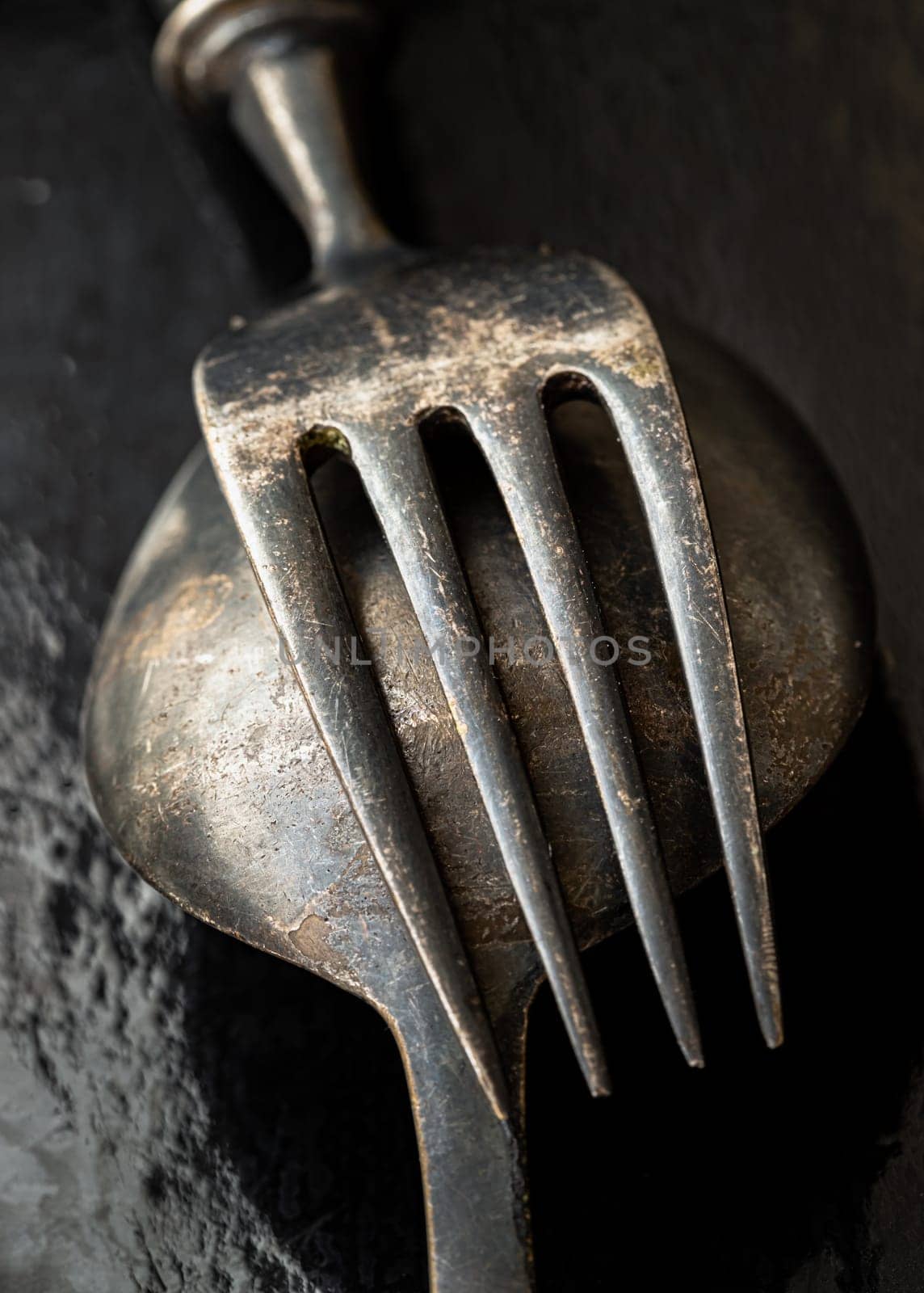 Close-up of Ancient worn vintage cutlery on the dark background. Crossed black metal spoon and fork in dark tone, Highlighting its texture and design, use it as your Wallpaper, Poster and Copy space Selective focus.