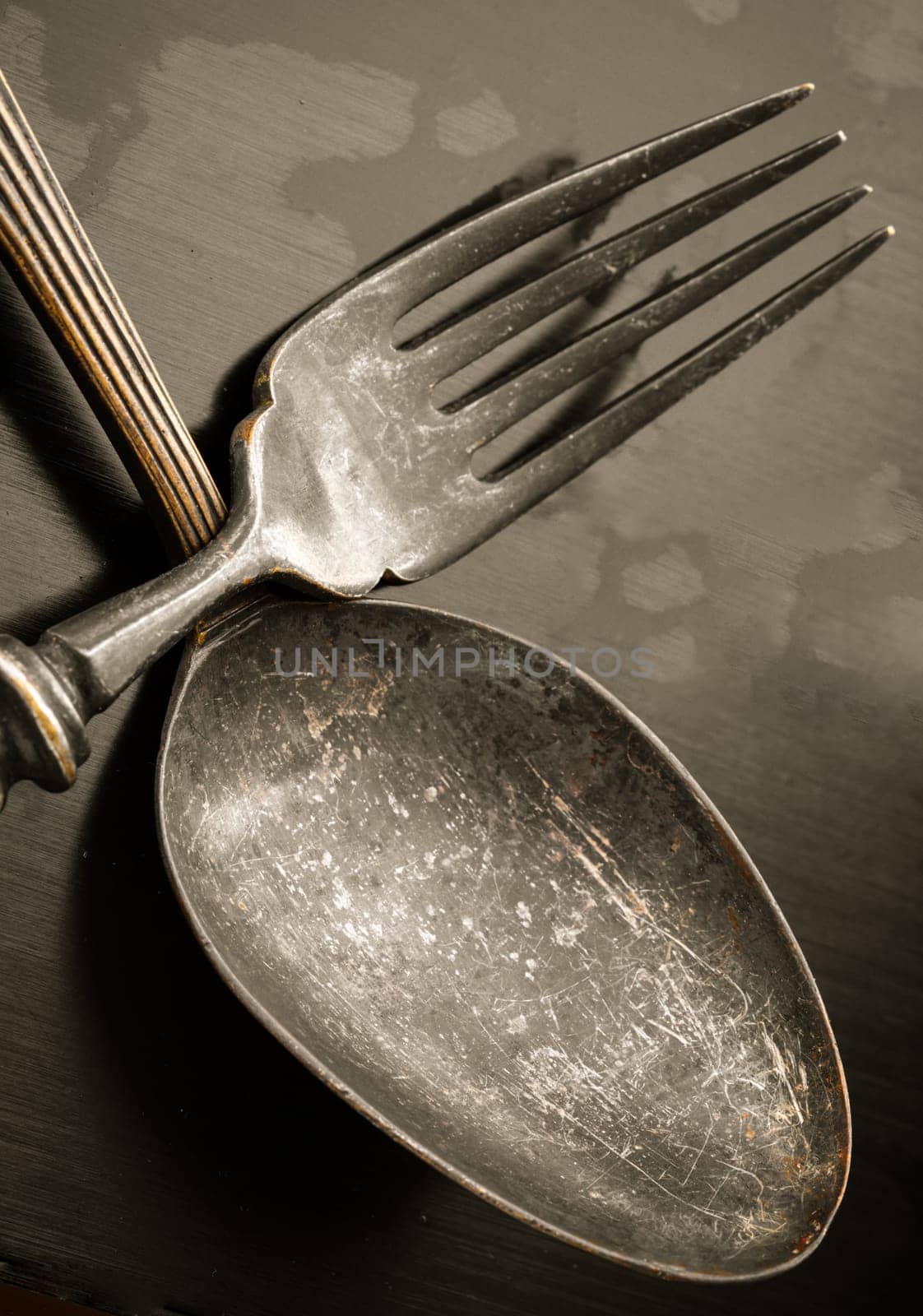 Close-up of Ancient worn vintage cutlery on the dark background. Crossed black metal spoon and fork in dark tone, Highlighting its texture and design, use it as your Space for text, Design, Wallpaper and Poster, Selective focus.