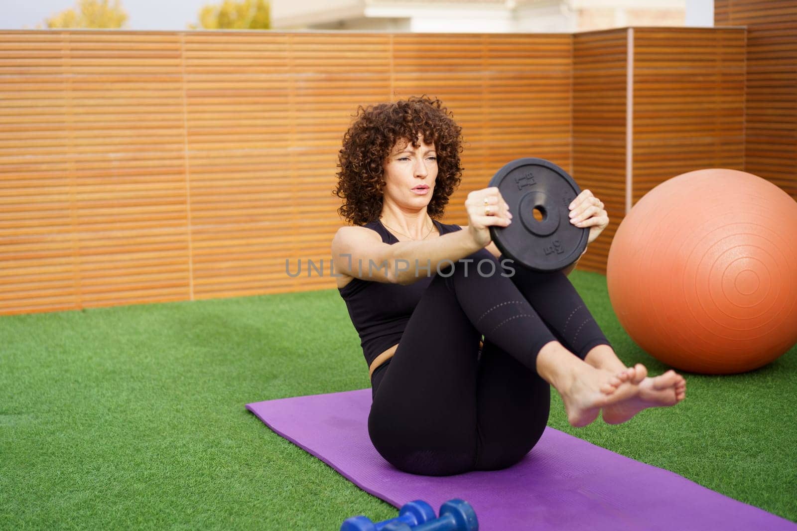 A dedicated woman performs an intense core workout on an outdoor yoga mat with a weight plate, emphasizing the importance of fitness and a healthy lifestyle for overall wellbeing
