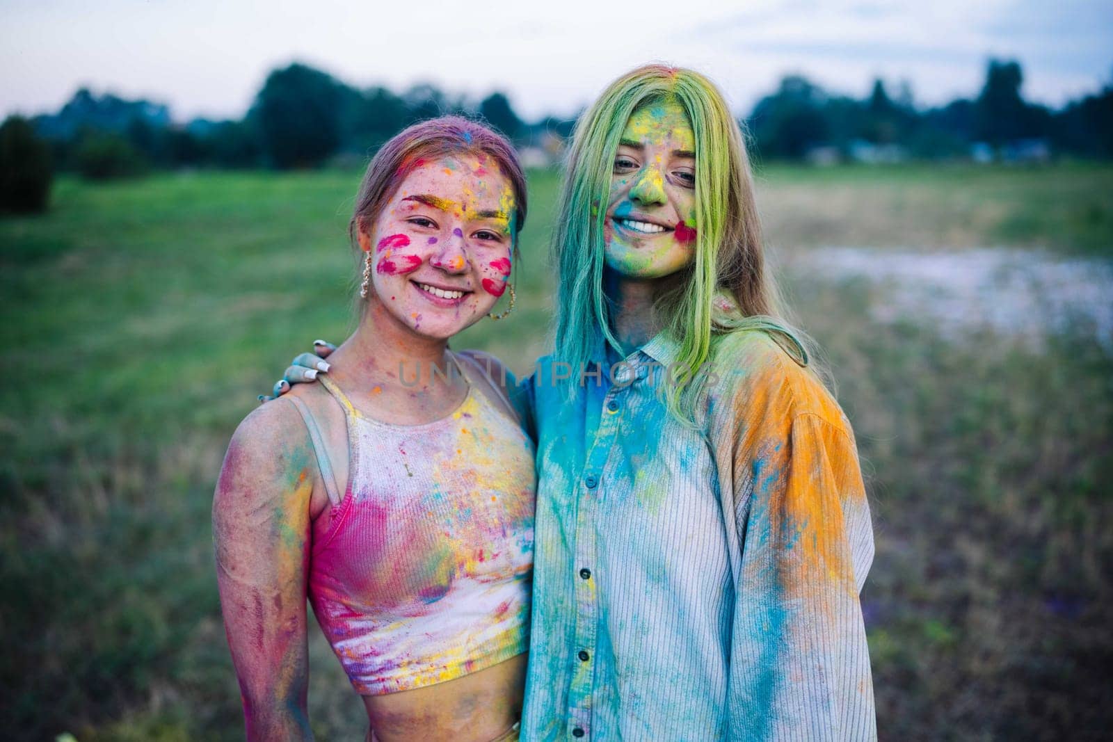 Two joyful young women, covered in vibrant holi powder, celebrating the colorful festivities outdoors with laughter and friendship