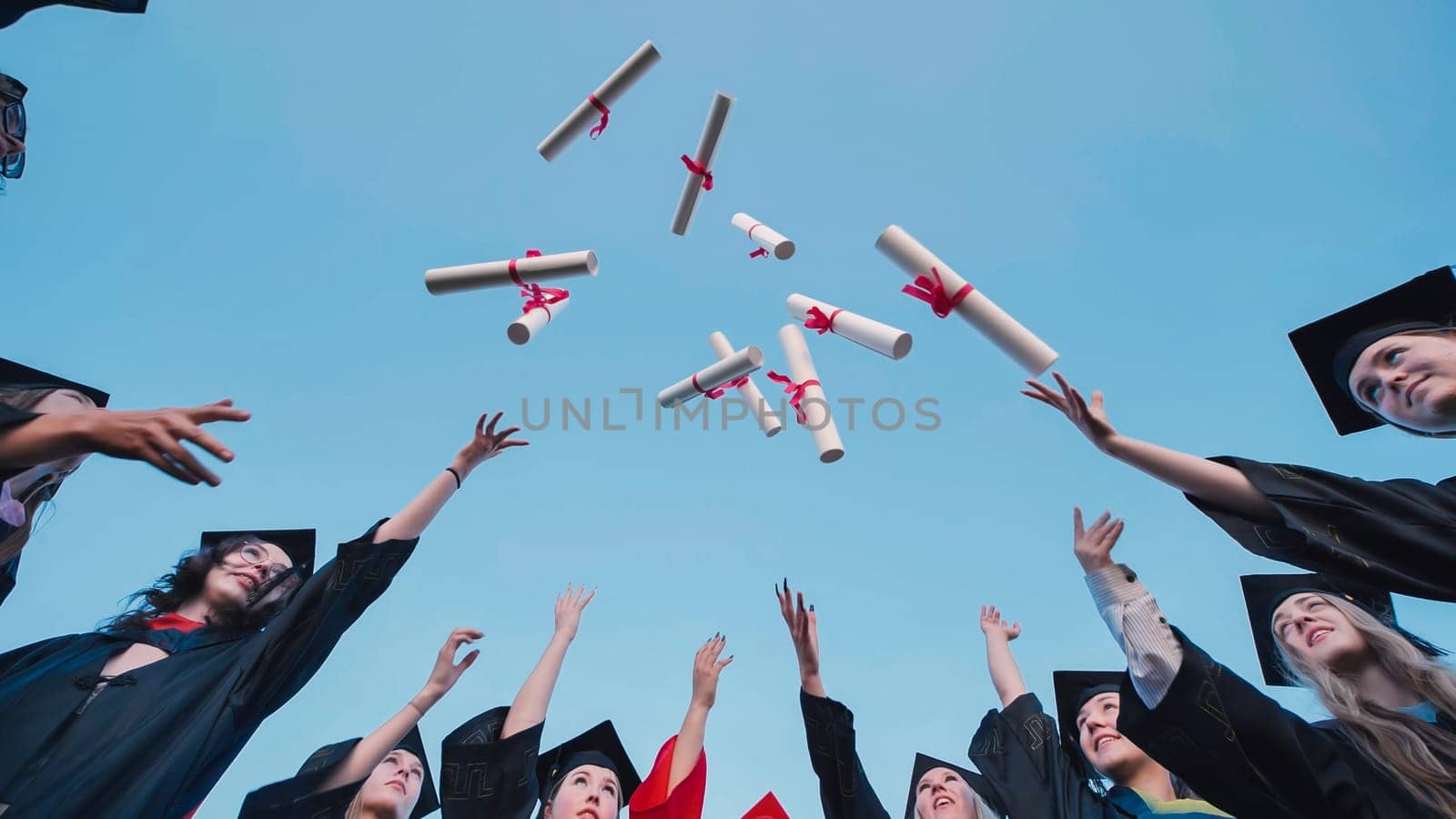 Group of students wearing graduation gowns throwing diplomas in the air, celebrating their academic achievement