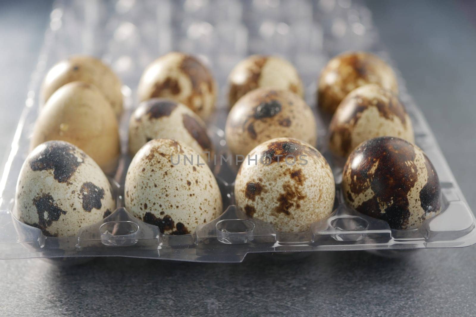 Different colored quail eggs are neatly placed in a plastic carton.