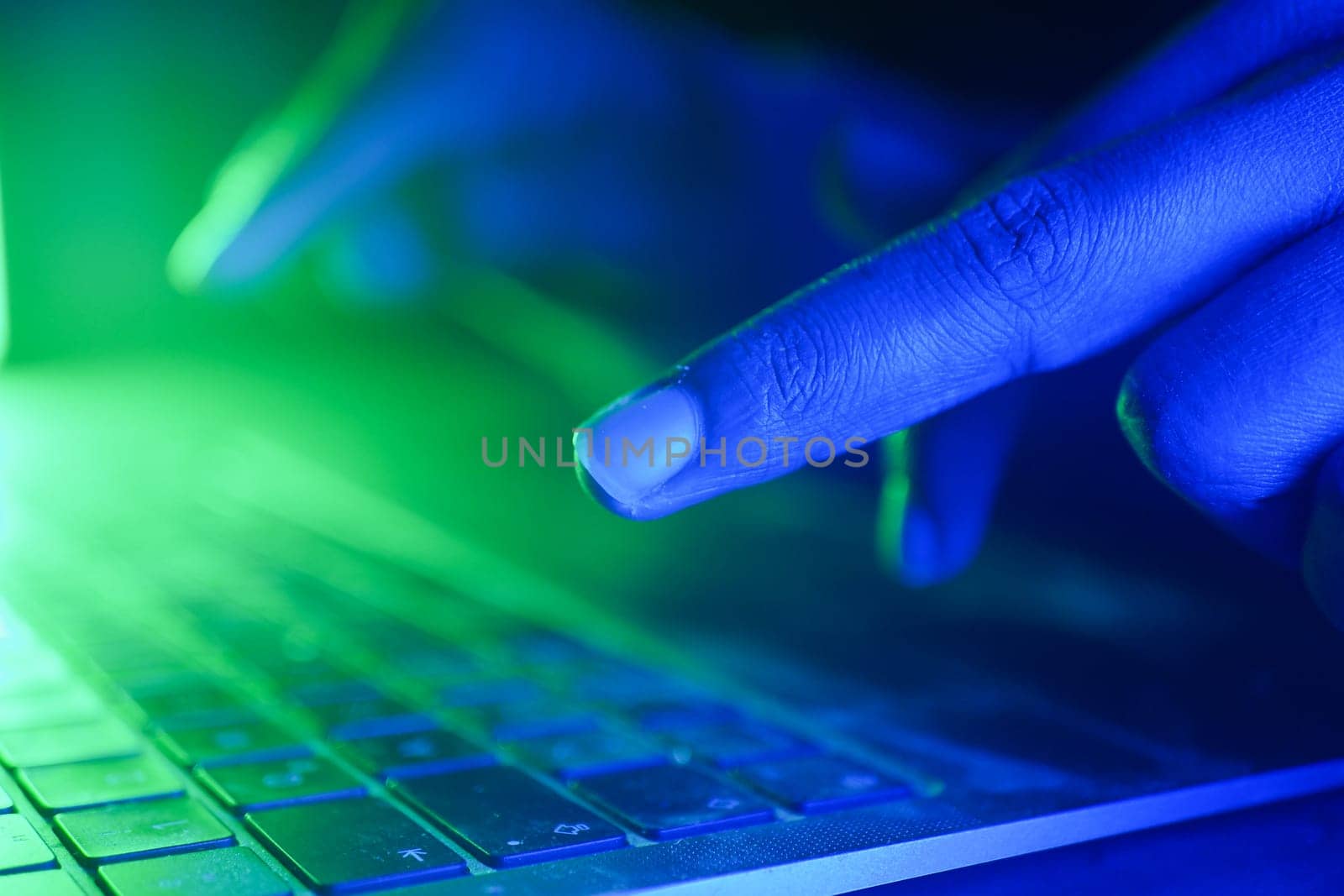 hacker typing on keyboard illuminated by green and blue light.