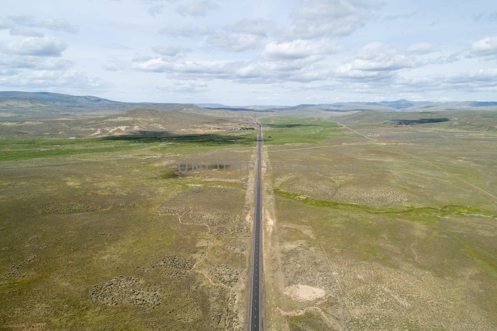 A long road stretches across a dry, barren landscape. The sky is cloudy, and the sun is barely visible. The emptiness of the scene gives off a sense of loneliness and isolation