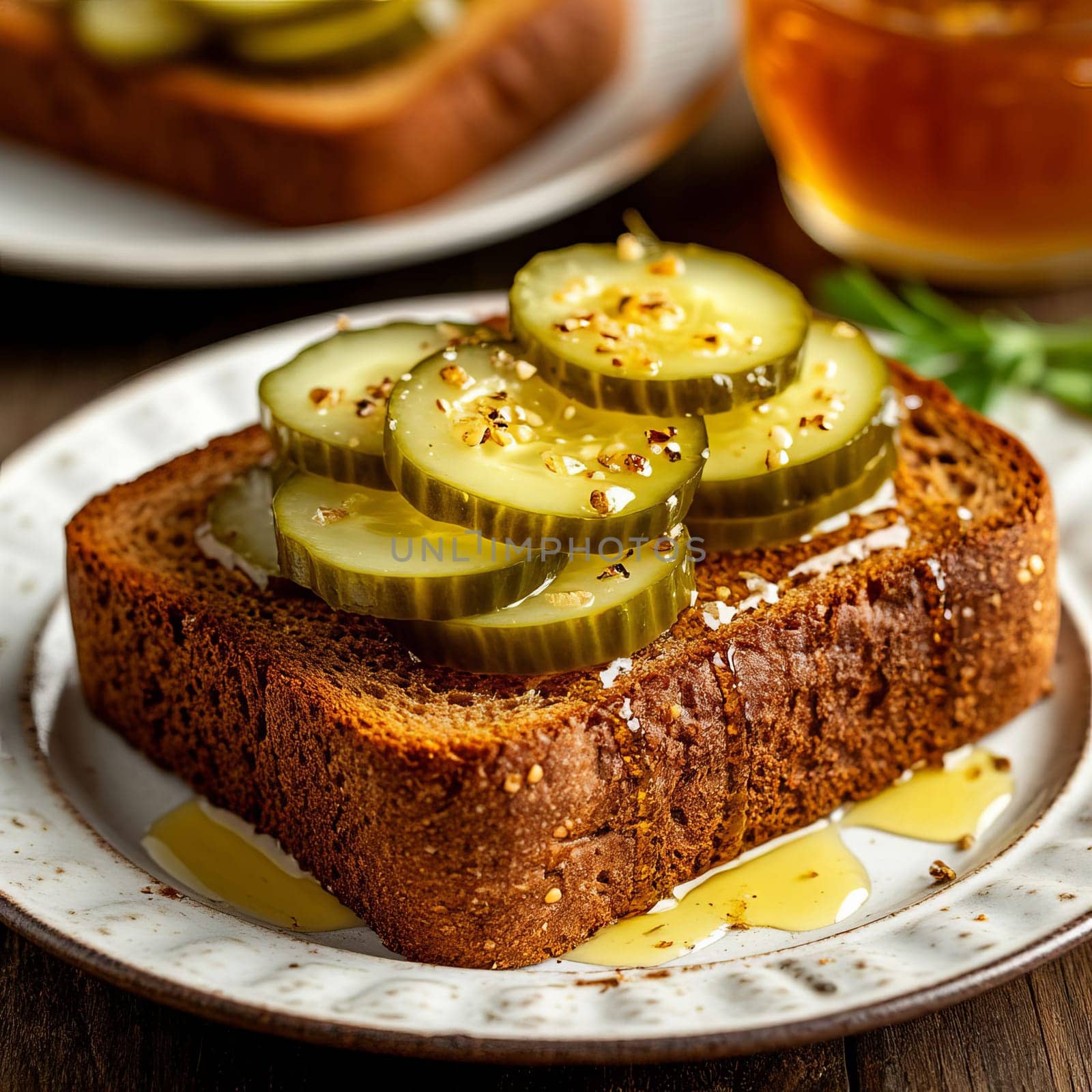 Sliced pickles are arranged on a piece of dark rustic bread, drizzled with honey. Contrasts of savory and sweet flavors.