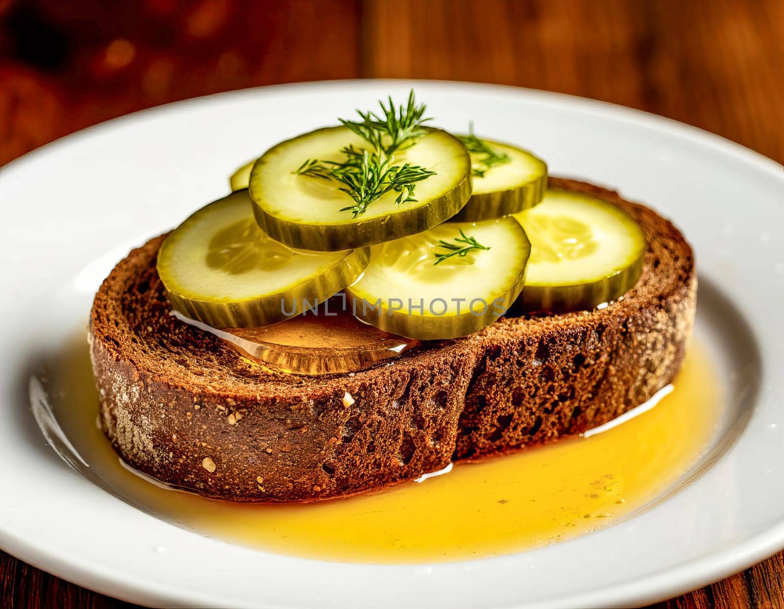 Sliced pickles are arranged on a piece of dark rustic bread, drizzled with honey. Contrasts of savory and sweet flavors.