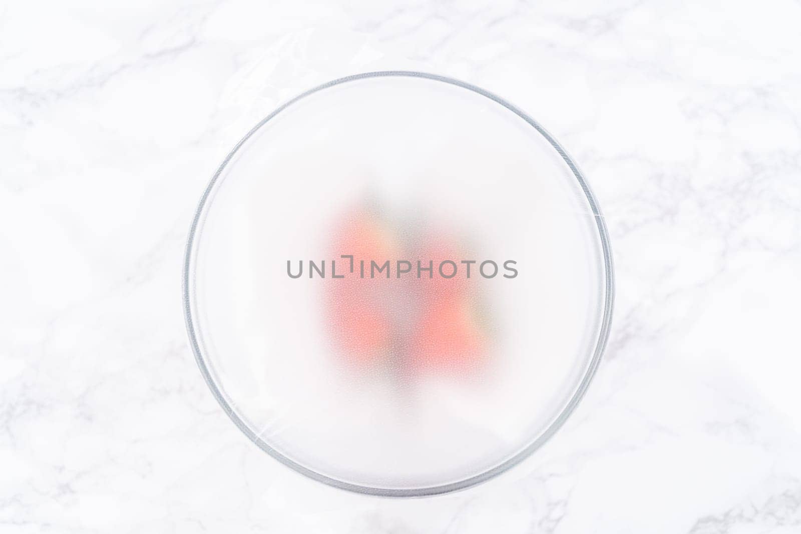 Strawberries, freshly washed and dried, are neatly stored in a glass bowl lined with a paper towel and securely covered with plastic wrap to maintain freshness.