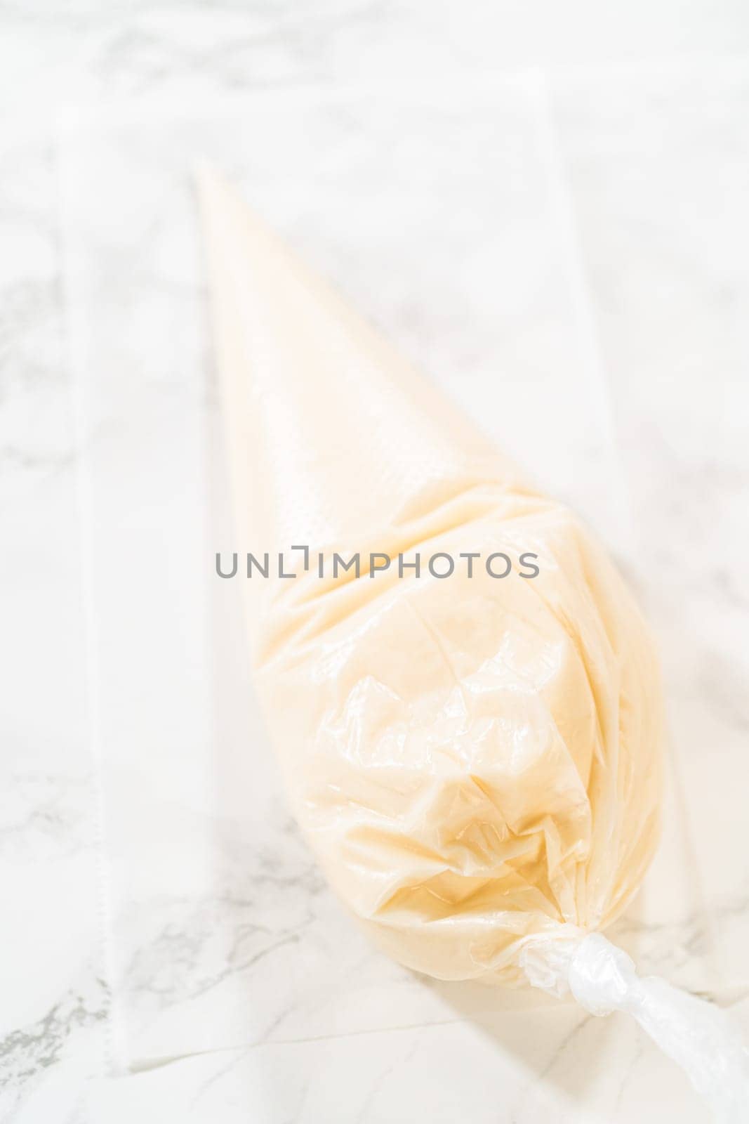 A single piping bag filled with white royal icing resting on a marble surface, ready for decorating festive mitten cookies.