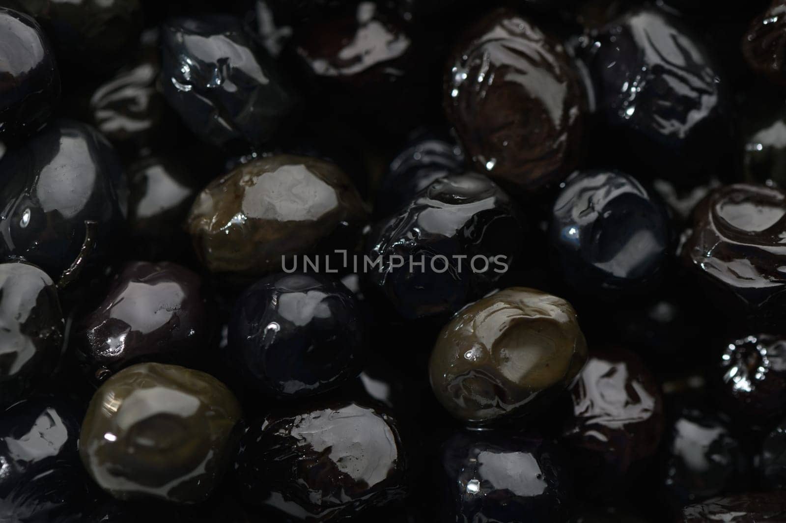 Glistening black olives rest closely together, reflecting light in a rich display of earthy tones. Harvested from local orchards, they symbolize nature's culinary treasures, ready for use.