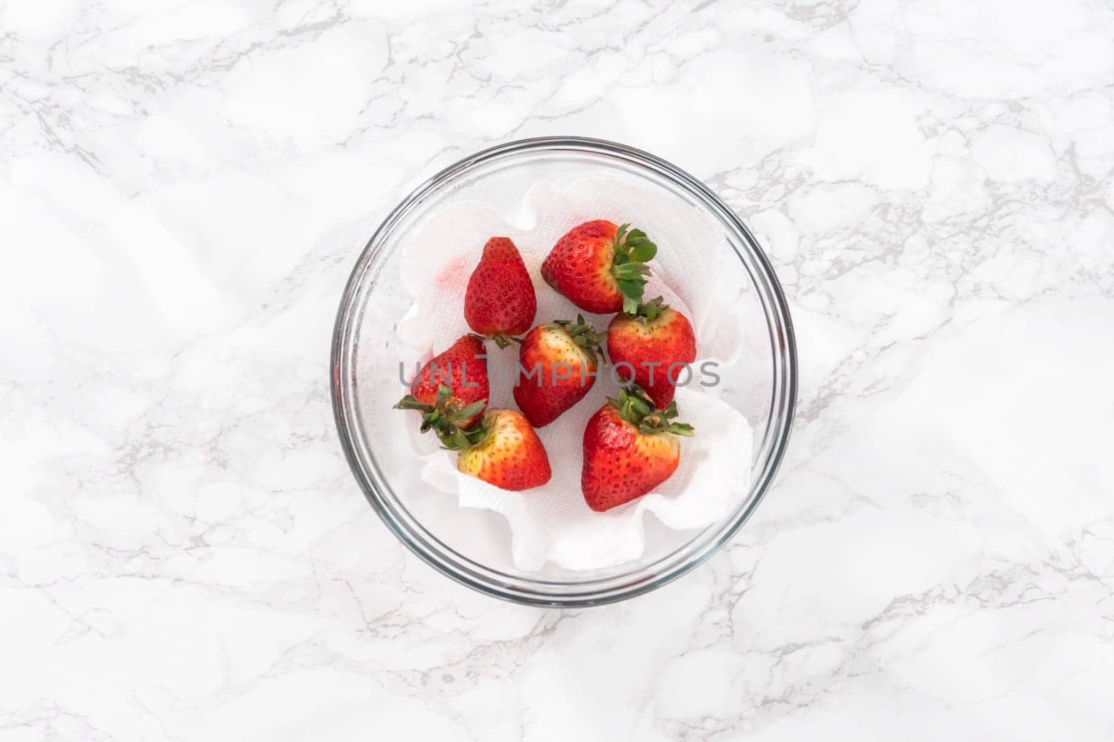 Freshly washed and dried strawberries are carefully arranged in a glass bowl lined with paper towel, ready for snacking or further use.