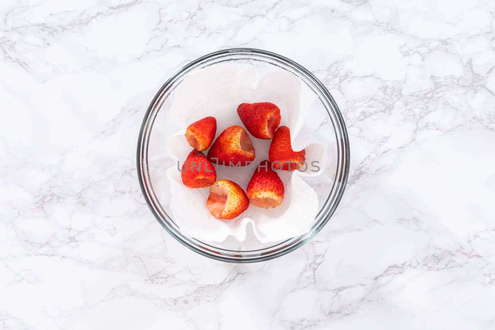 Freshly washed and dried strawberries are carefully arranged in a glass bowl lined with paper towel, ready for snacking or further use.