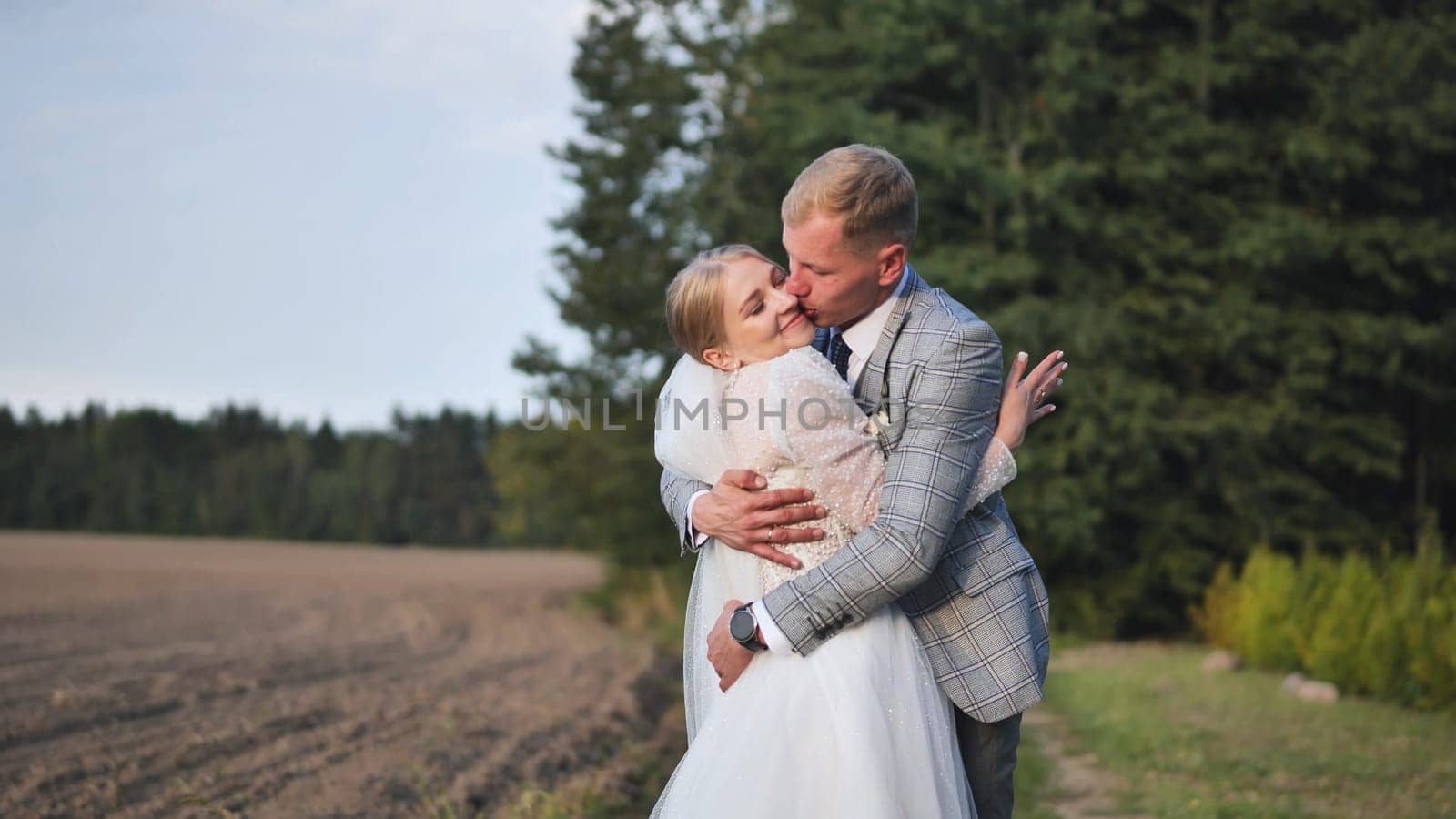 Newlywed couple kissing and embracing on their wedding day, celebrating their love in a picturesque natural setting near a forest