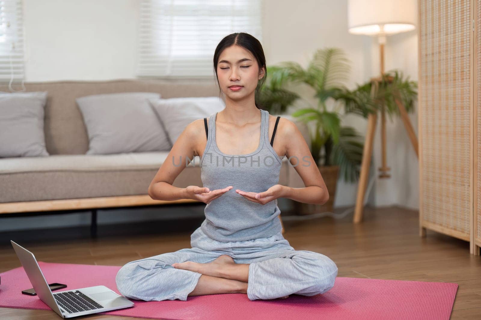 In a peaceful setting, a woman sits cross-legged, focuses on her breath, and practices mindfulness, creating a tranquil atmosphere in her living room.