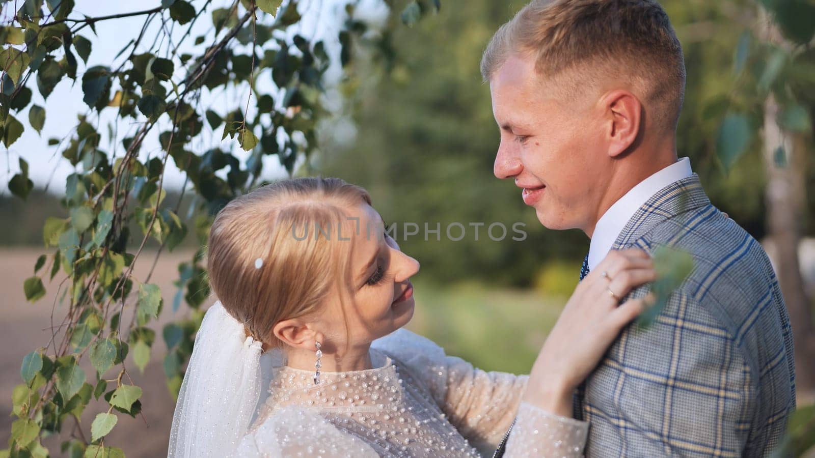 Newlyweds embracing and smiling under birch branches, enjoying a romantic moment on their special day