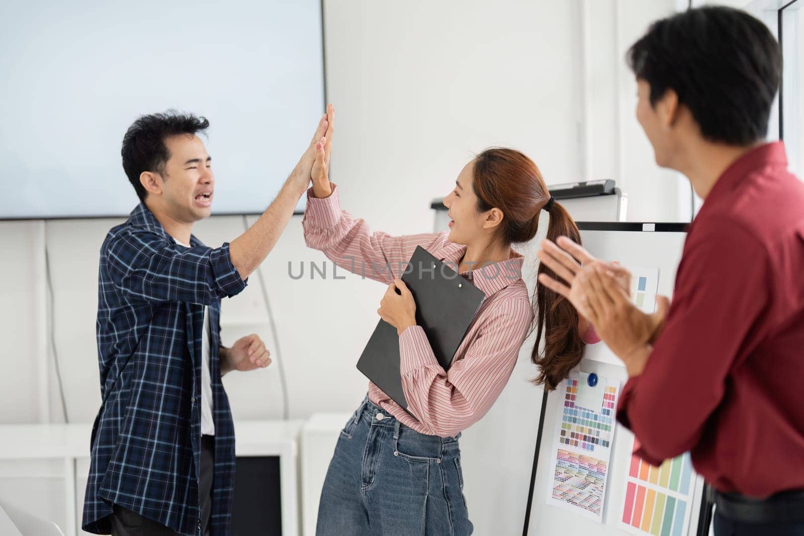 In a vibrant office setting, two colleagues enthusiastically high-five each other while a third team member shares in the joyful moment, showcasing teamwork and camaraderie.