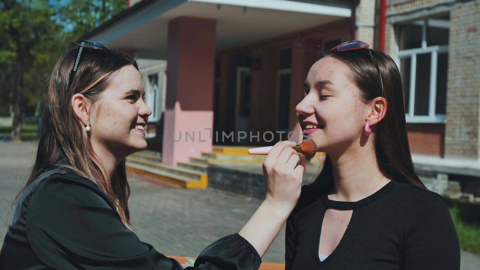 Two teenage girls having fun applying makeup during a school break, enjoying their time together outside