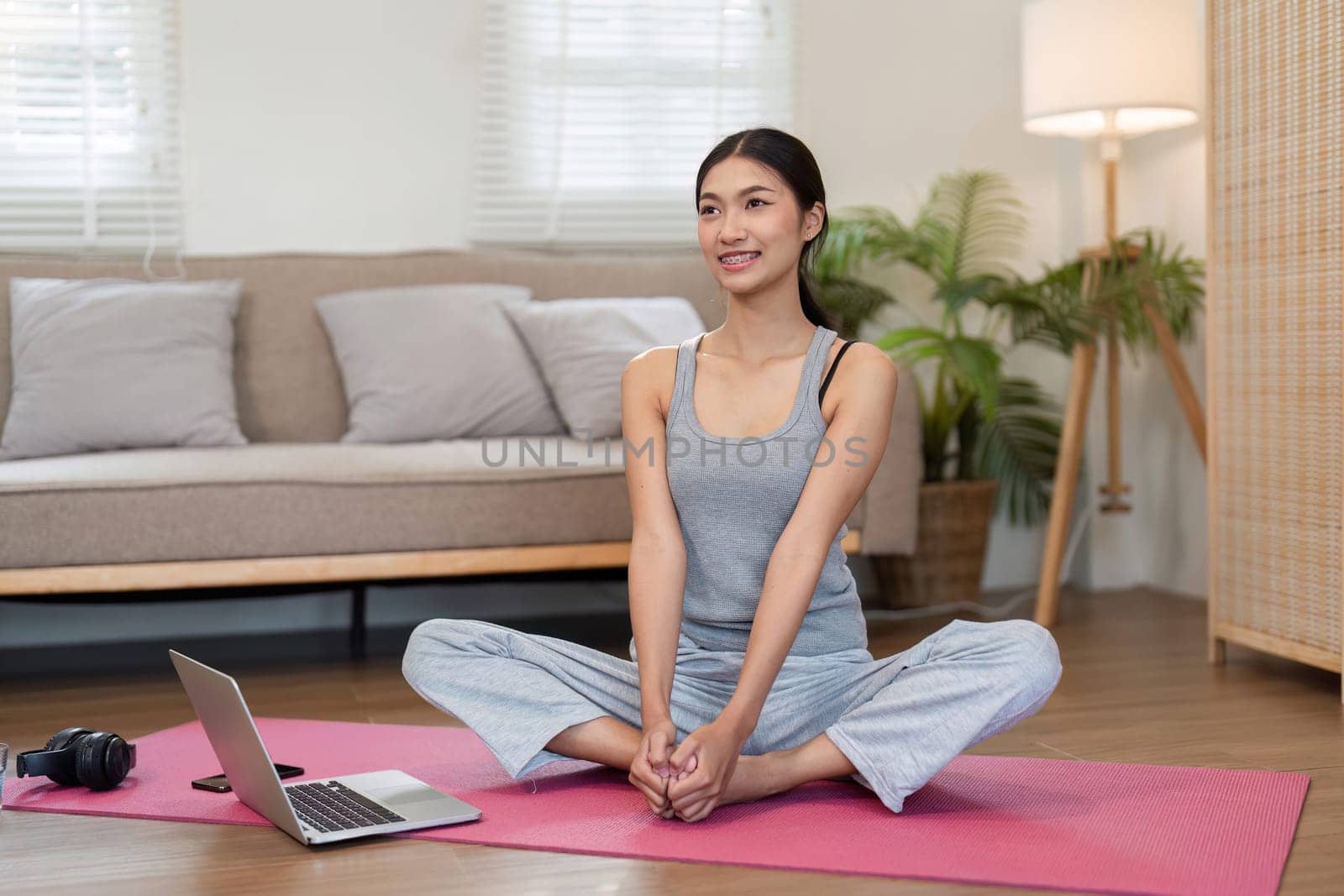 A smiling woman sits on a yoga mat, engaging in relaxation and mindfulness exercises with a focus on her breathing and overall well-being.