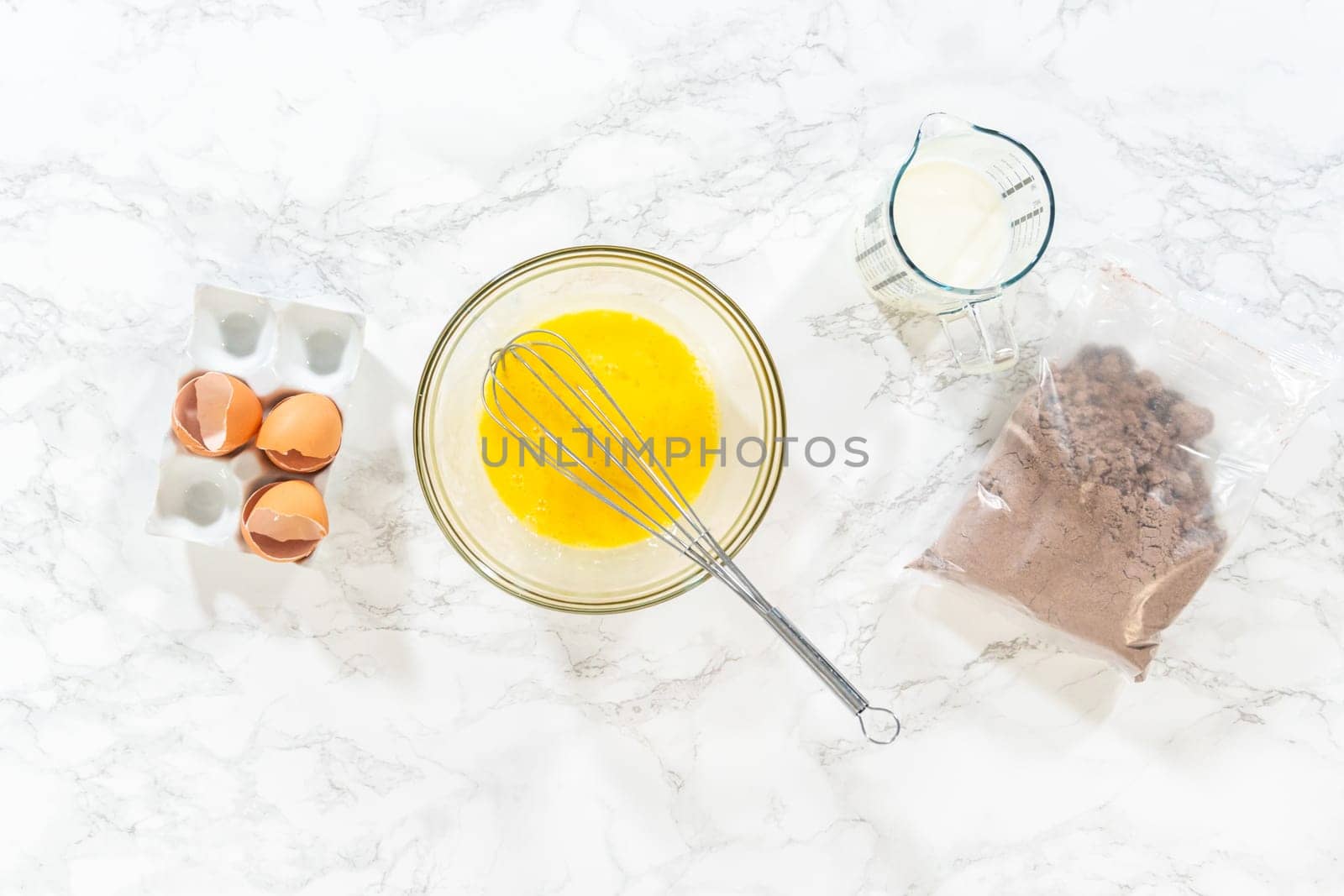 Flat lay. In the process of creating mouthwatering chocolate cupcakes, the first step involves meticulously mixing the ingredients in a glass mixing bowl to make the perfect batter.