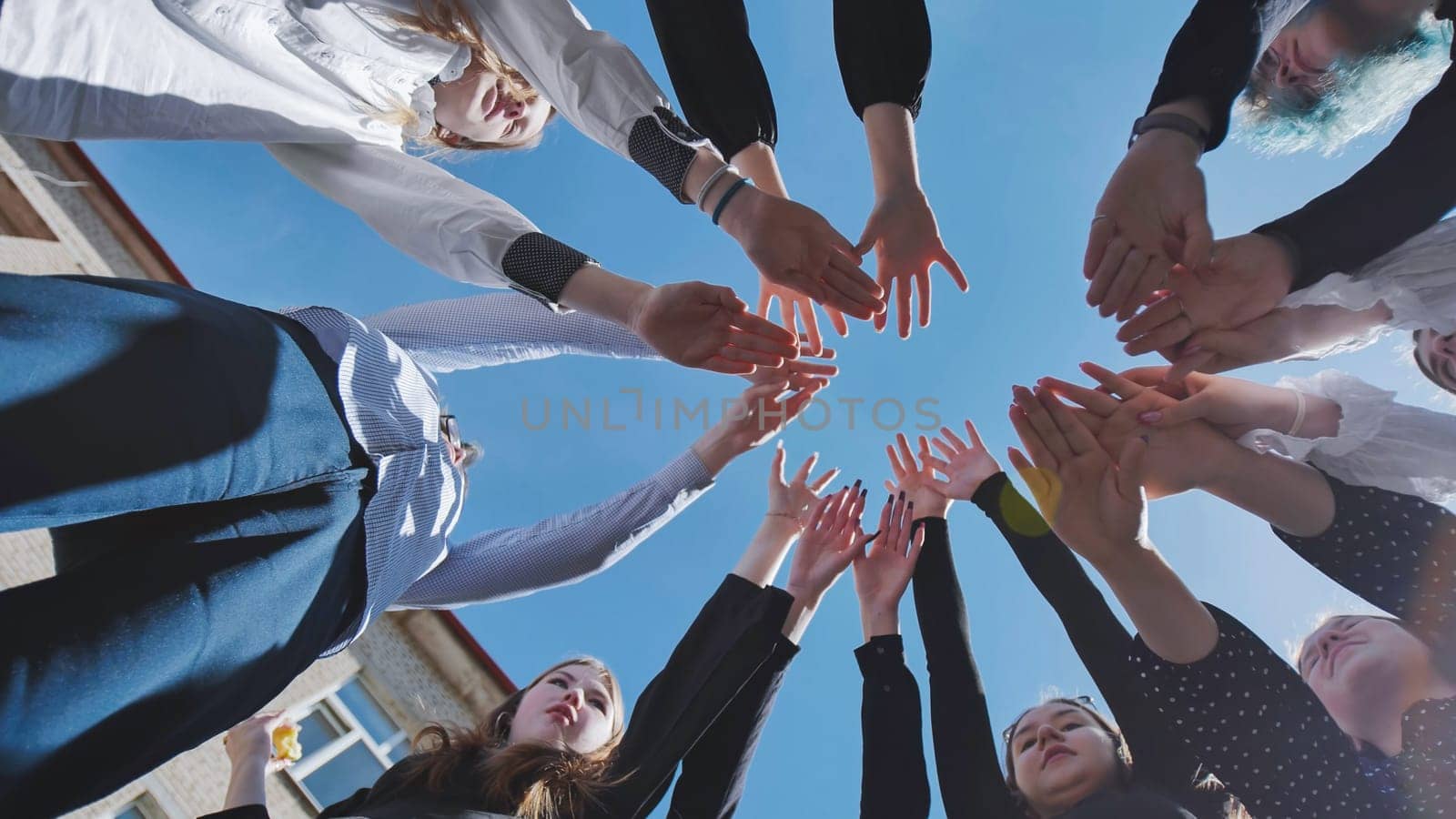Group of students forming a circle with their hands against a clear blue sky, demonstrating collaboration and togetherness