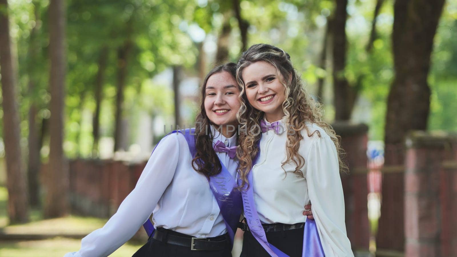 Two recent female graduates embracing on their last day of school, exuding joy in a beautiful green park. Embracing their success, eagerly anticipating what lies ahead