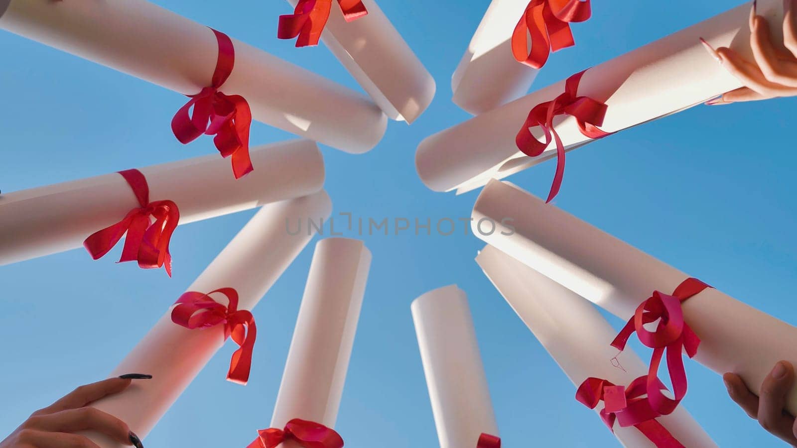 Graduates join their diplomas in a circle against the sky