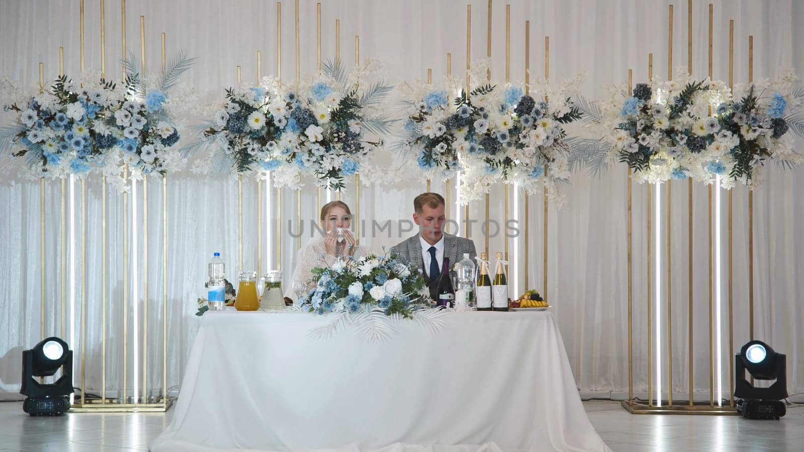 Newlyweds sitting at their wedding table, adorned with elegant floral arrangements, enjoying a special moment during their reception