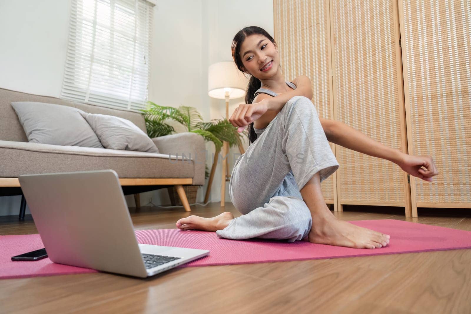 In a comfortable home setting, a woman engages in yoga stretching while using a laptop for online guidance.