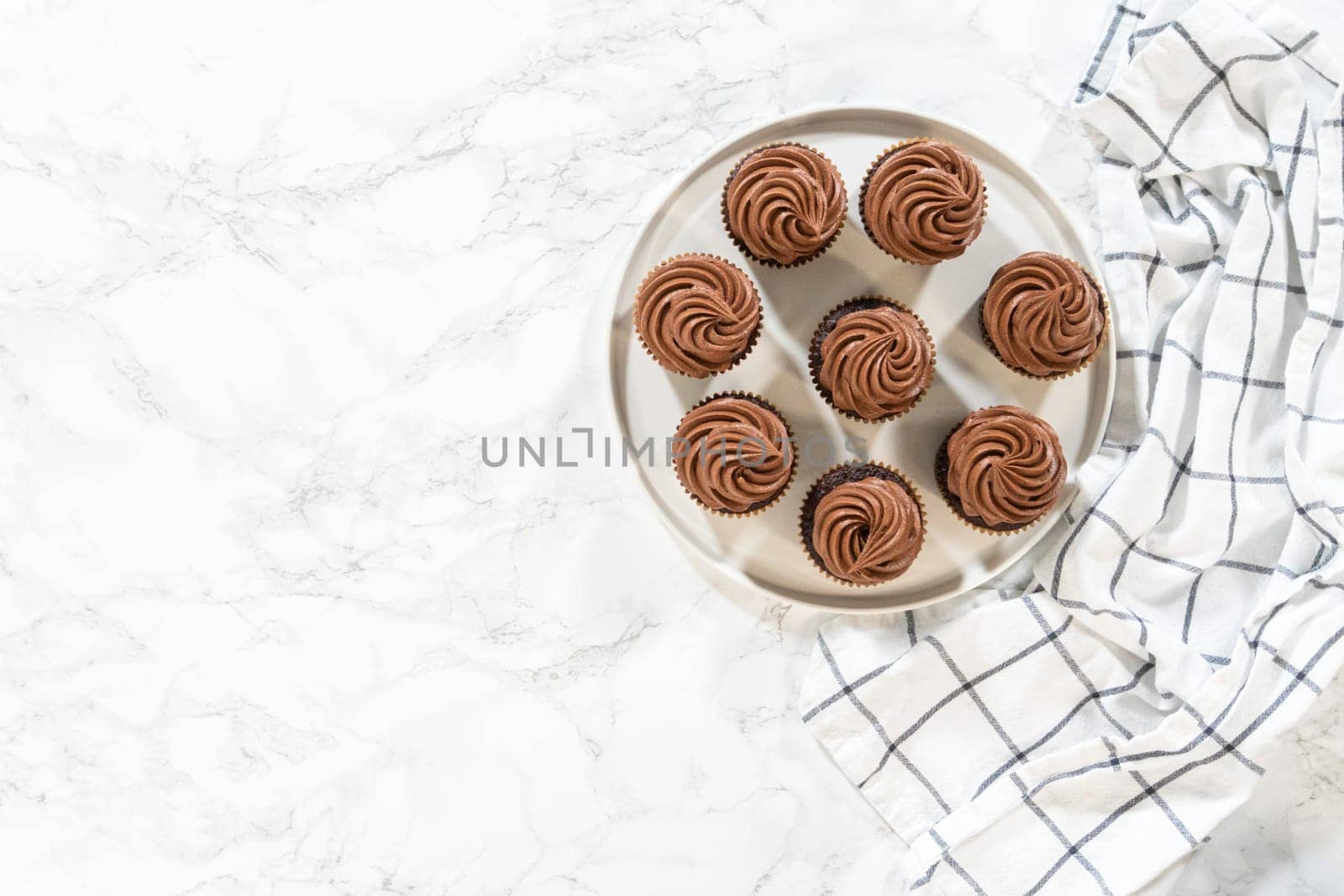 Flat lay. Freshly baked cupcakes have been masterfully infused with rich caramel and adorned with velvety chocolate frosting, all elegantly presented on a pristine white serving plate.