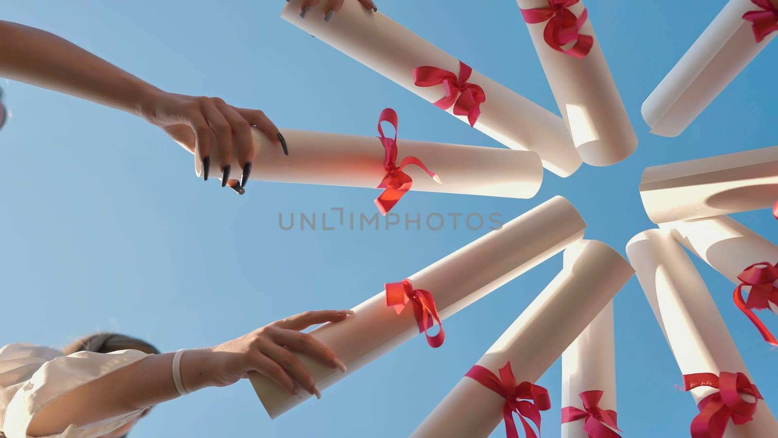 Group of students celebrating their graduation by holding their diplomas together towards a clear blue summer sky