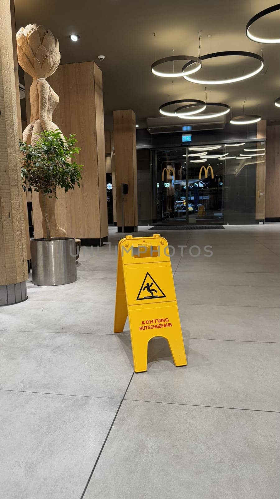 22.03.2025 Germany: Indoor McDonalds Setting Featuring a Caution Sign and Wooden Decorative Art Piece. Modern interior of McDonalds with clean floors, wooden decor, and a bright yellow caution sign emphasizing safety.