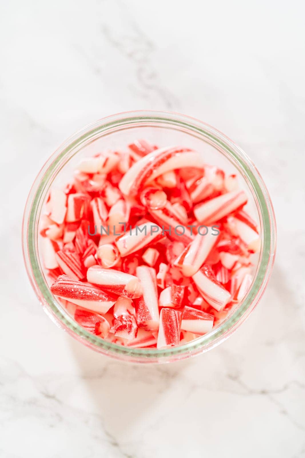 A glass jar filled with crushed candy canes, displayed on a marble countertop, showcasing their vibrant red and white stripes for holiday dessert decoration and baking.