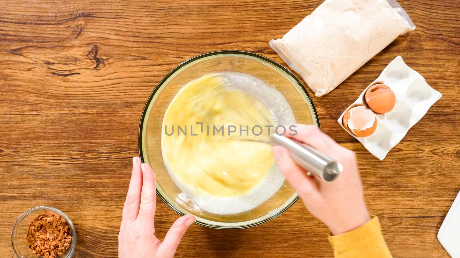 Flat lay. In a glass mixing bowl, a large hand whisk expertly blends the ingredients for a delectable gingerbread bundt cake with caramel frosting.