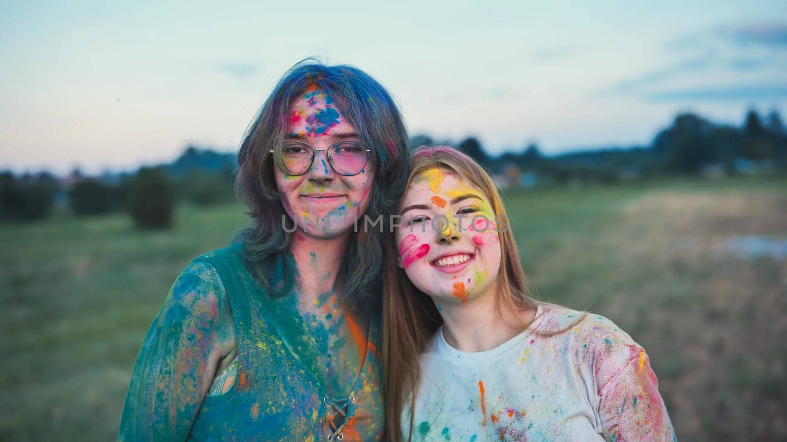 Two joyful young women, adorned in colorful holi powder, share a loving embrace at a festival, reveling in the bond of friendship and the vibrant hues of the celebration