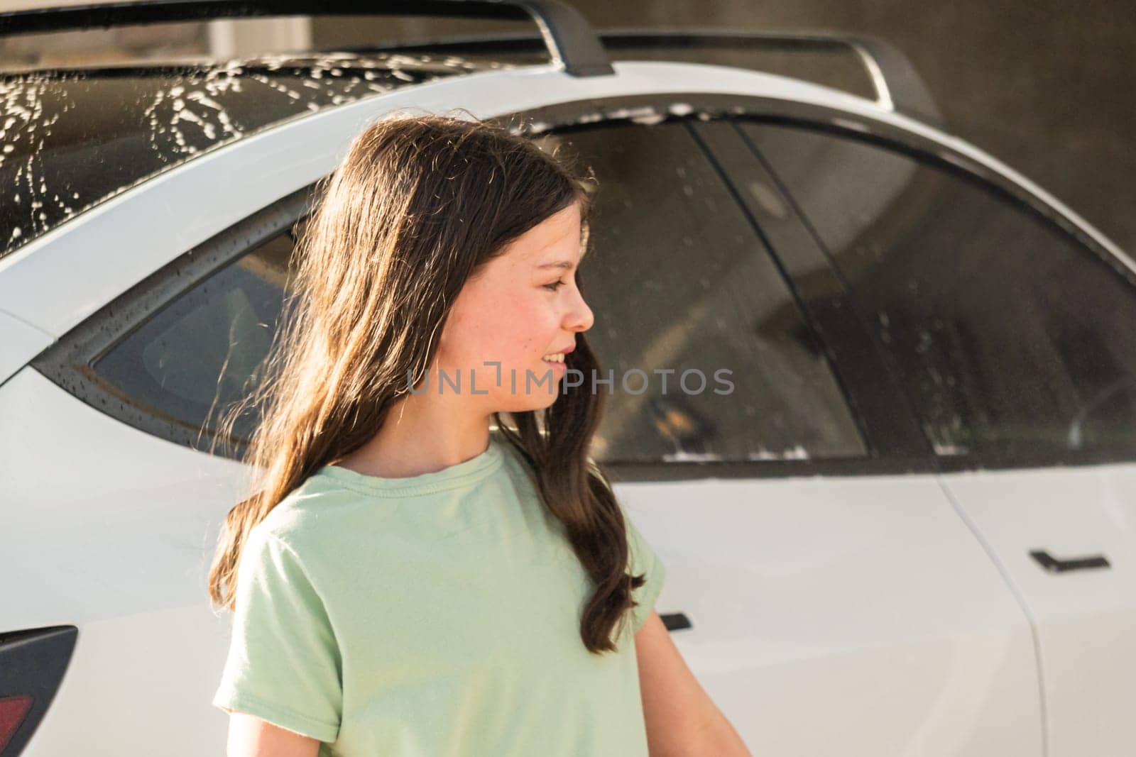 A young girl enthusiastically assists in washing the family's electric car in their suburban driveway.
