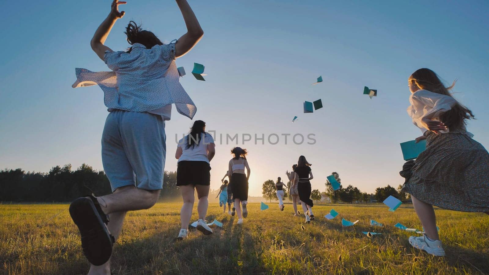 Graduation girl running in the background of the sunset and throwing her hat and notebooks.