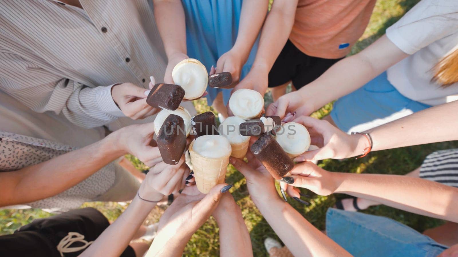 School friends are holding ice cream cones and chocolate covered ice cream bars, enjoying a sweet treat together outdoors