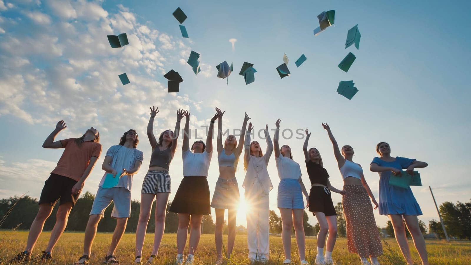 Happy students tossing notebooks into the air to celebrate their graduation against a sunset backdrop