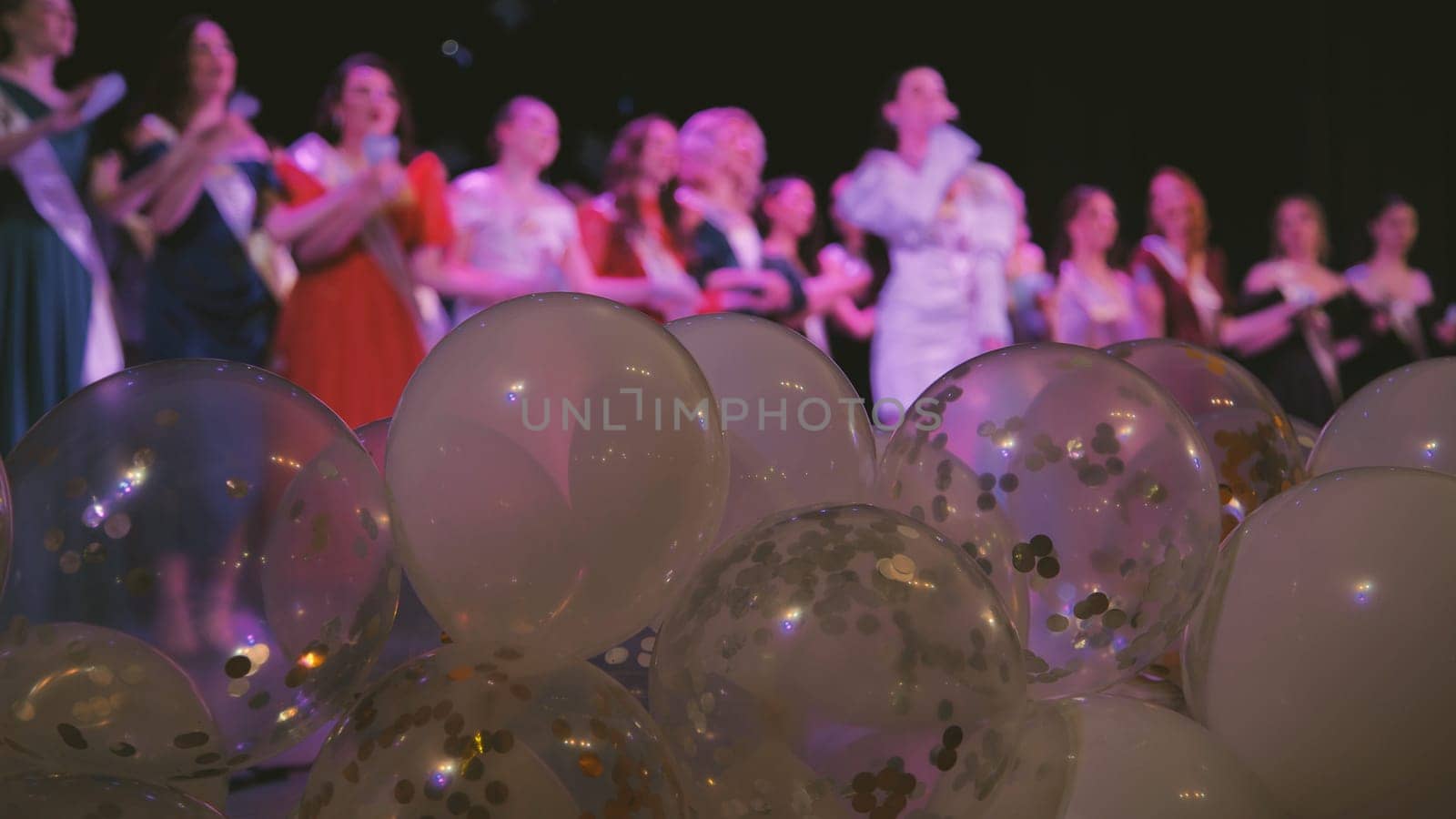 White and transparent balloons decorated with confetti during a school event with a group of clapping friends in the background