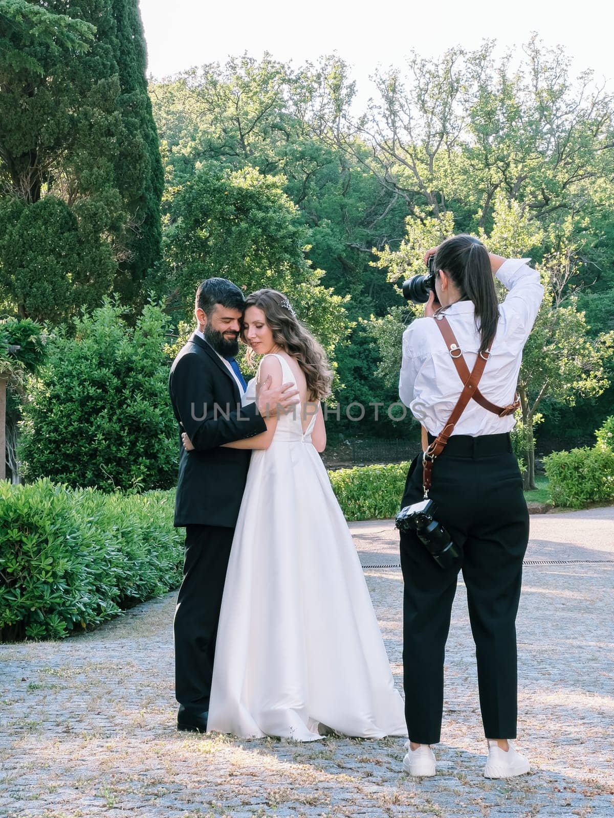 Photographer girl photographs bride and groom hugging in the garden. High quality photo