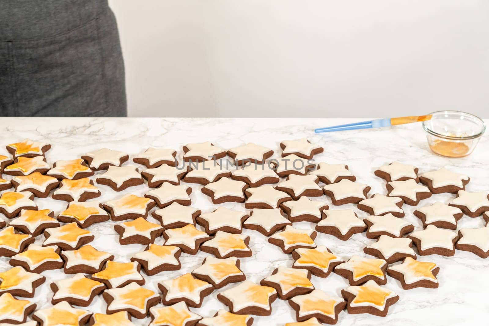 A wide spread of golden-decorated gingerbread star cookies arranged on a white surface, highlighting their intricate royal icing and elegant gold luster dust finish.