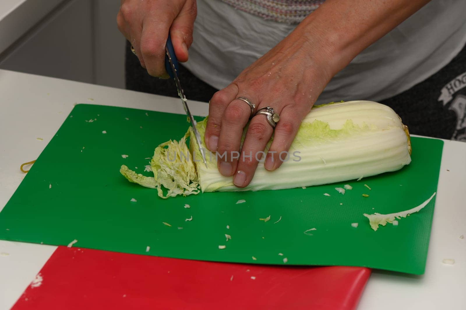 Hands skillfully slice a fresh head of cabbage on a bright green cutting board. The kitchen buzzes with the joy of preparing a healthy meal, filled with fresh ingredients.
