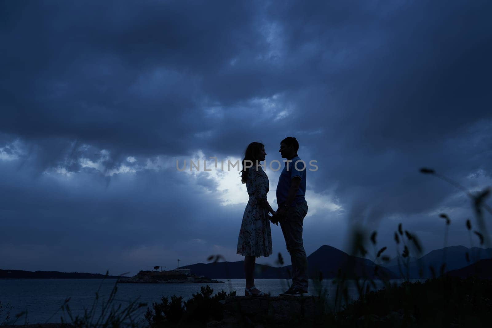 Man and woman stand holding hands by the sea against a dark sky. High quality photo