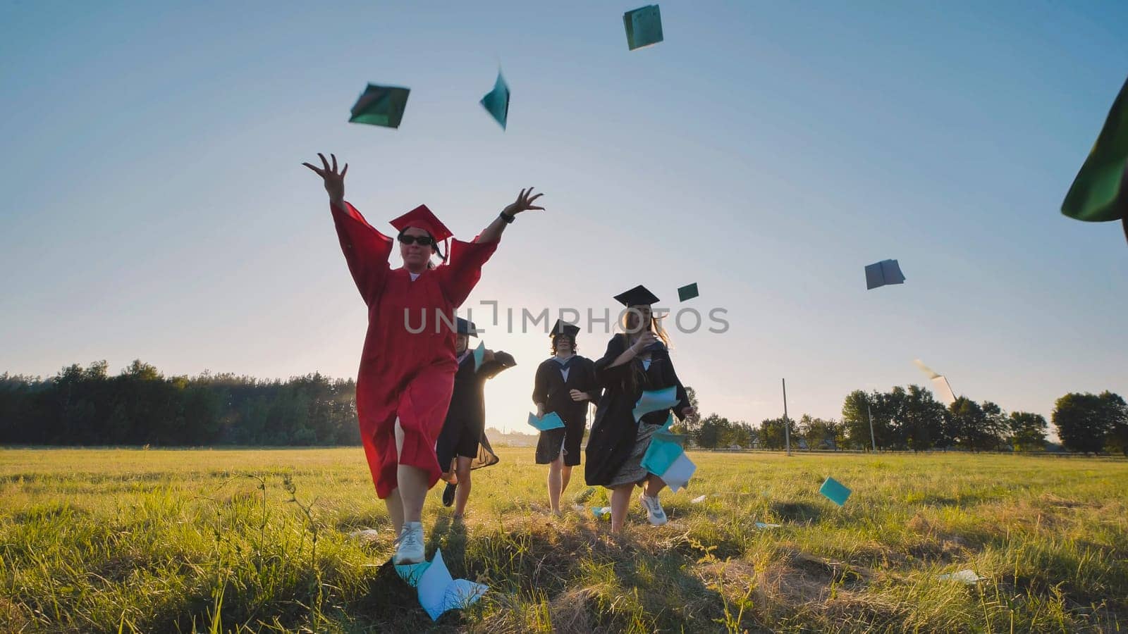 Group of cheerful graduates wearing gowns and caps throwing books in the air, celebrating their academic achievement