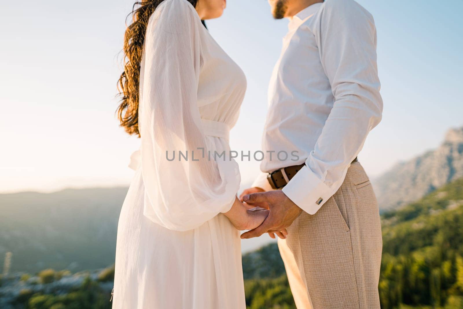 Bride and groom hold hands on the mountain. Cropped. Faceless. High quality photo
