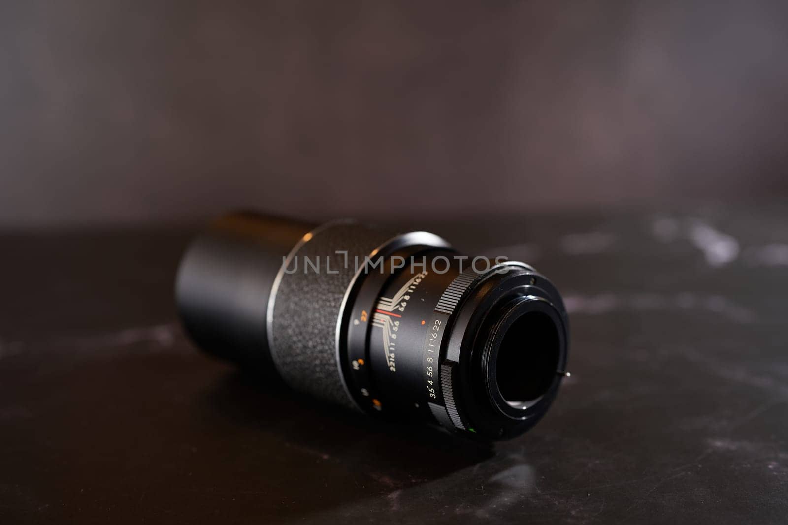 Vintage automatic telephoto lens lies on a black table. Back view. High quality photo